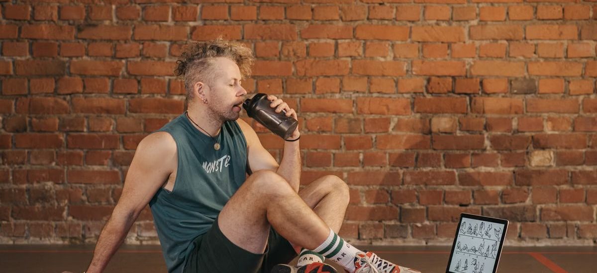 Athletic man sitting on exercise mat with water bottle, taking a break from workout, in a rustic indoor setting.