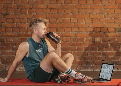 Athletic man sitting on exercise mat with water bottle, taking a break from workout, in a rustic indoor setting.
